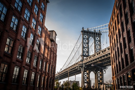 Picture of Manhattan bridge seen from a narrow alley enclosed by two brick buildings on a sunny day in summer
